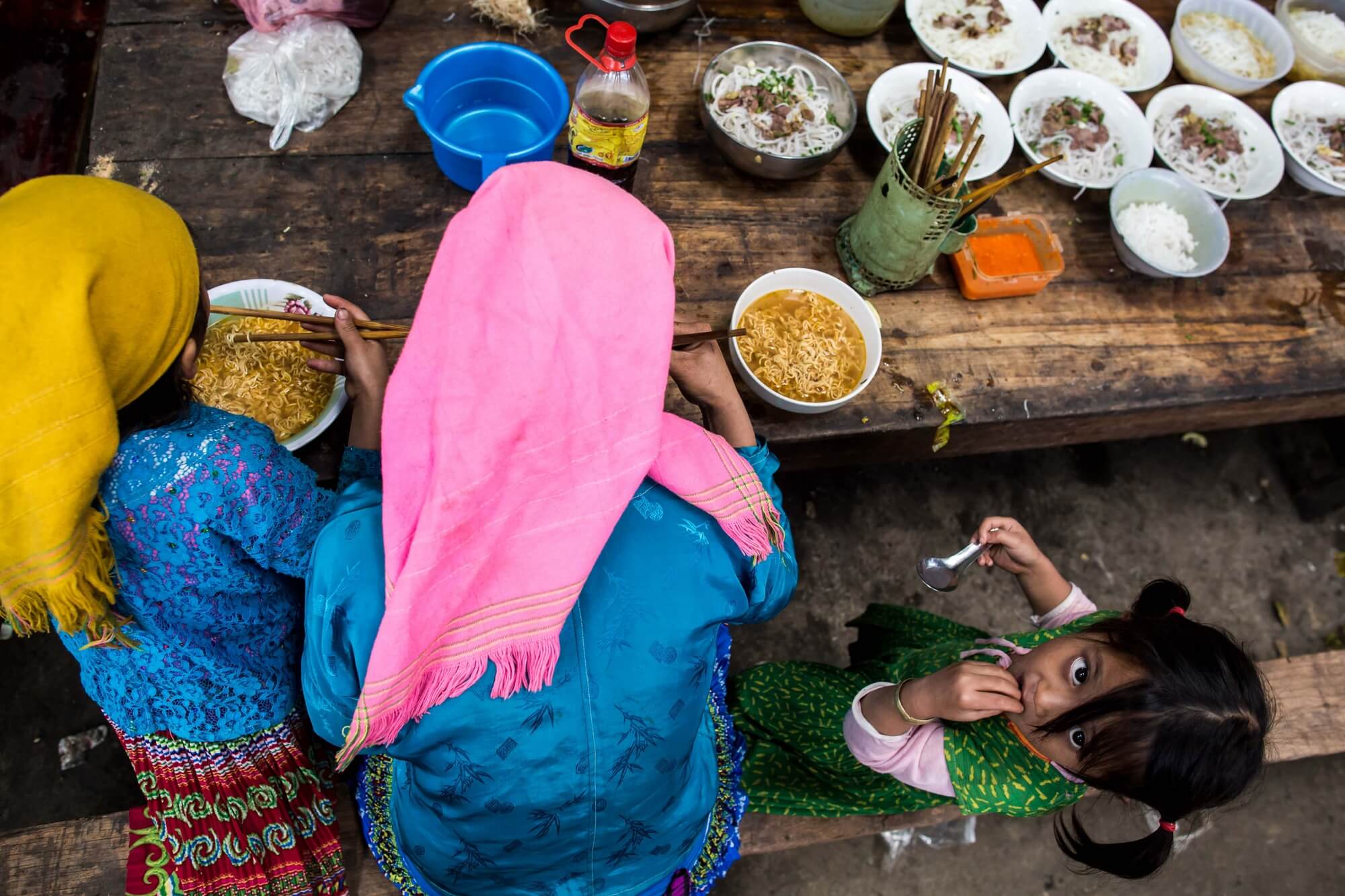 Two Vietnam Minority women eating soup with curious child